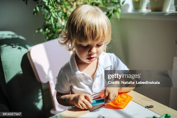 creative expression: blond toddler boy engaged in modeling clay, dough art in bright home. - moulant photos et images de collection