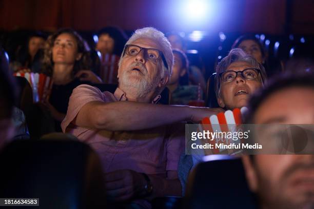 mid-shot de casal sênior assistindo a um filme dentro do teatro - indian couple in theaters - fotografias e filmes do acervo