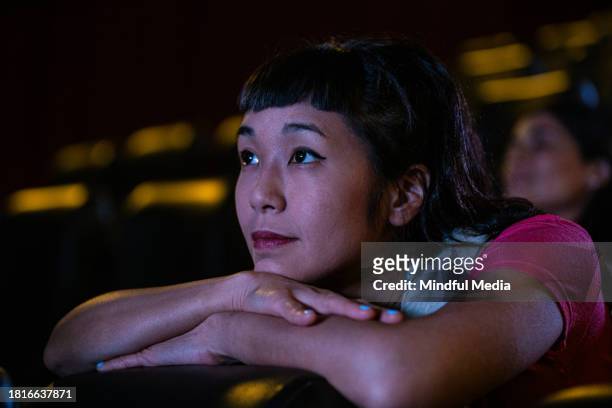 side view of young asian american woman leaning on front seat while watching a film inside movie theater - indian couple in theaters stock pictures, royalty-free photos & images
