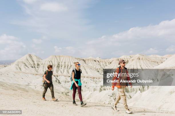 a group of people, a man and a woman with backpacks, walking through the desert against the backdrop of mountains in a sandy canyon of the altyn emel national park in kazakhstan. travel concept. - kazakistan foto e immagini stock