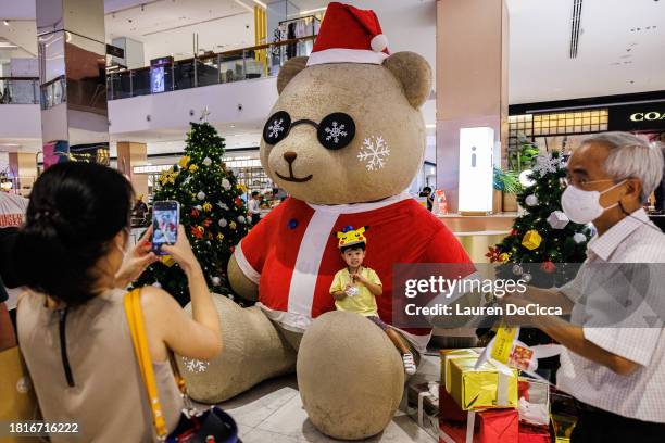 Little boy has his photo taken while wearing a Pikachu hat and sitting on a Santa Claus bear at Central World Shopping Mall during a holiday kick off...