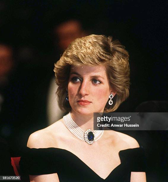 Diana, Princess of Wales, wearing a midnight blue velvet, off the shoulder evening dress designed by Victor Edelstein, a sapphire, diamond and pearl...
