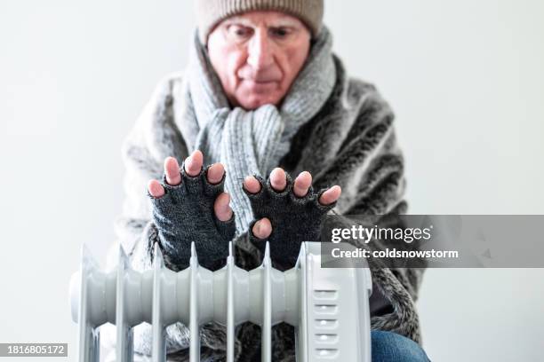 cold senior man warming his hands over electric heater at home - fingerless glove stock pictures, royalty-free photos & images