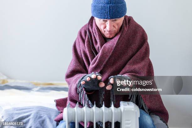 cold senior man warming his hands over electric heater at home - frozen man stockfoto's en -beelden