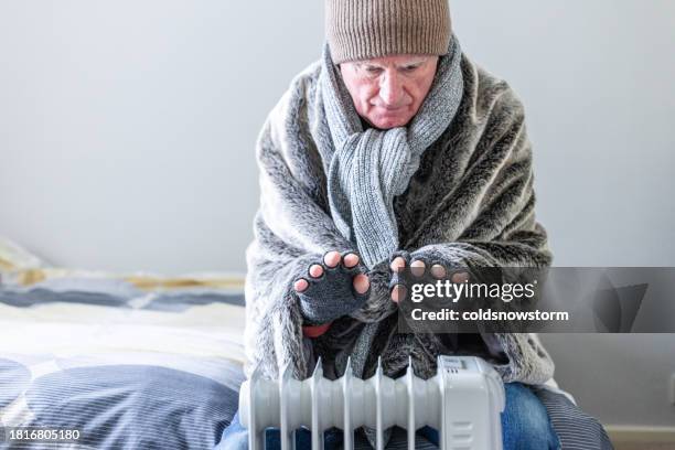 cold senior man warming his hands over electric heater at home - fingerless glove stock pictures, royalty-free photos & images