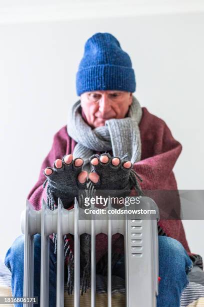 cold senior man warming his hands over electric heater at home - fingerless glove stock pictures, royalty-free photos & images
