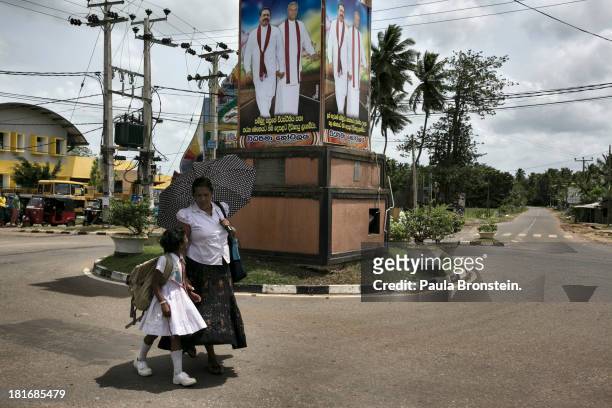 Woman walks her daughter home from school past a poster of President Mahina Rajapaksa in his home town of Weerakeitya, Sri Lanka, July 8, 2013. War's...
