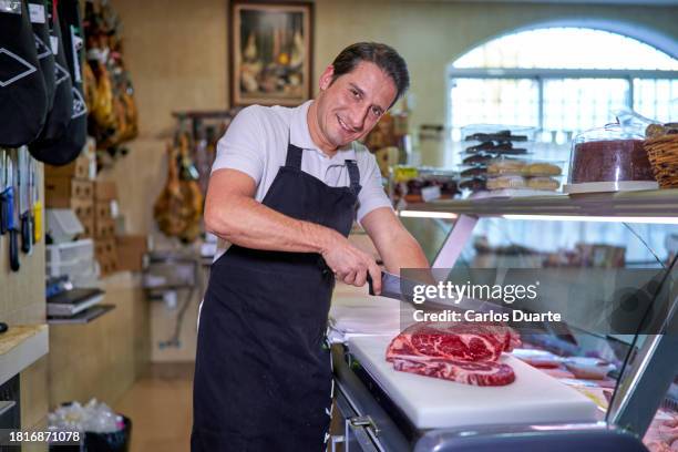 retrato de un carnicero español mirando a la cámara cortando carne en una carnicería española - carnicero fotografías e imágenes de stock