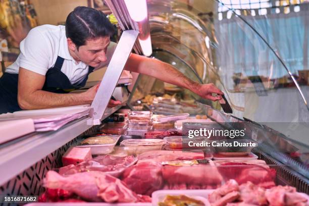 a spanish butcher from a neighborhood butcher shop places the price of a meat inside the refrigerator display - talhante imagens e fotografias de stock
