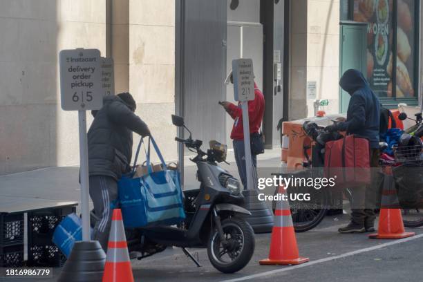 Worker arranges a giant cargo bag on his motorbike, two delivery workers check their phones, Instacart delivery order pickup area, the day before...