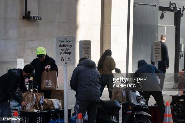 Two Wegmans employees arrange bags on a table for delivery workers, who are repacking bags for transport by motor and E-bike, Instacart delivery...