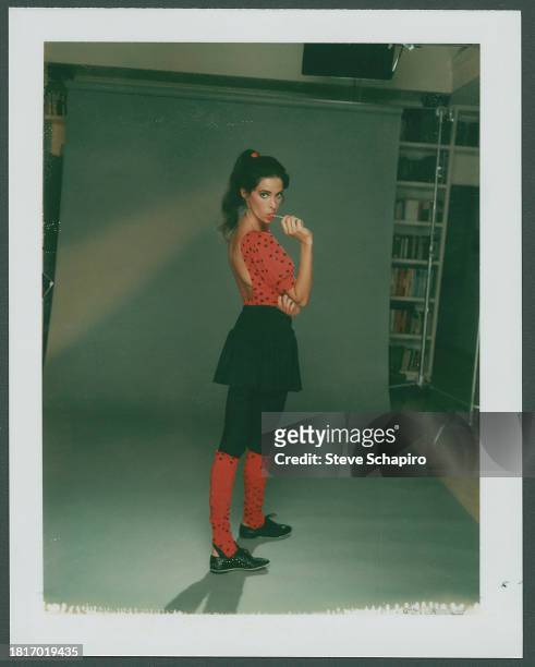 Portrait of American actress Connie Sellecca, in a red, polka dot top, dark skirt and tights, and red, polka dot socks, as she sucks a lollipop, Los...