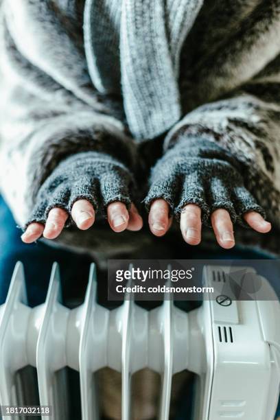 cold senior man warming his hands over electric heater at home - fingerless glove stock pictures, royalty-free photos & images