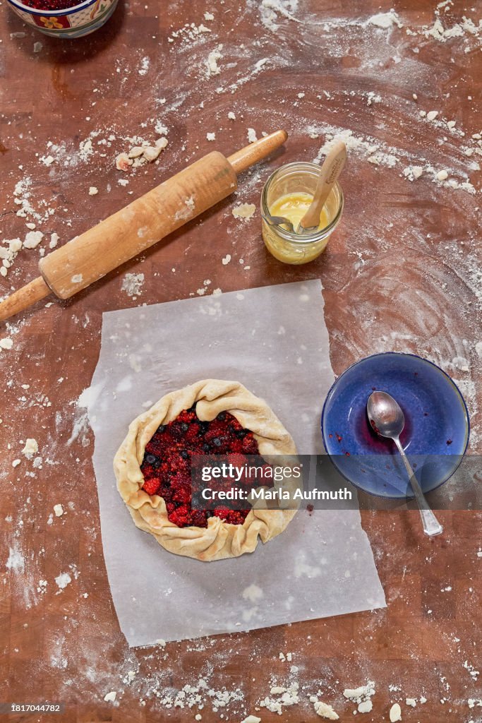 A foraged wild berry pie, galette on wax paper and a cutting board with rolling pen, egg wash, flour ready to be baked.