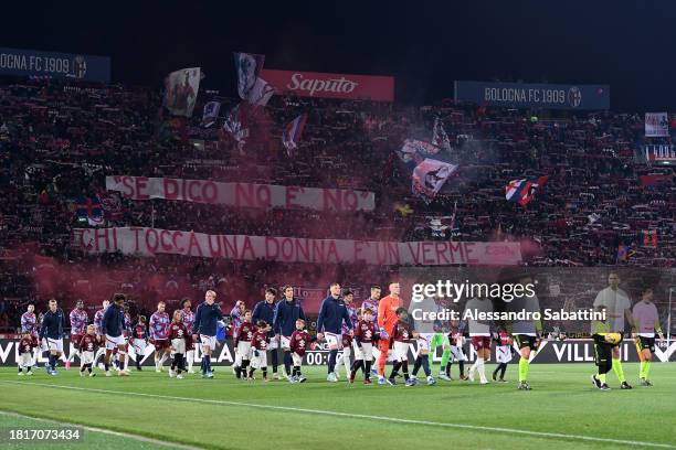 Players of Bologna and Torino walk out onto the pitch as fans hold up a sign in support of the #UNROSSOALLAVIOLENZA - the WeWorld Violence Against...