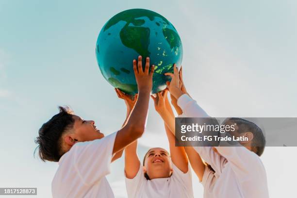 children holding a planet on the beach - earth day stock pictures, royalty-free photos & images