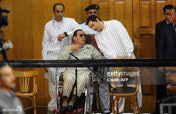 Egyptian toppled president Hosni Mubarak and his two sons Alaa and Gamal stand behind bars during their trial at the Police Academy on September 14,...