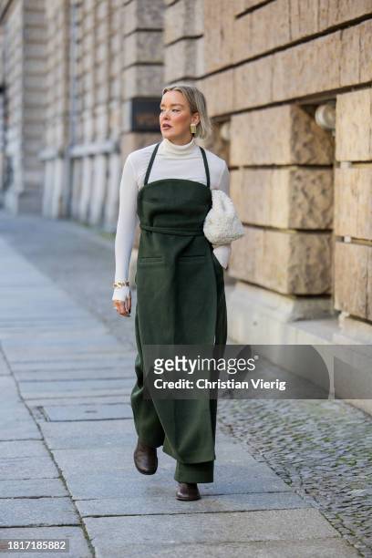 Tina Haase wears Karpova green wool pants & apron dress, white COS Teddy Clutch bag, white turtleneck, Zara heeled boots on November 27, 2023 in...