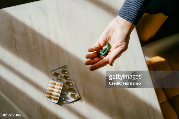 a woman standing at a table with green pills in her hand - hrt pill stockfoto's en -beelden