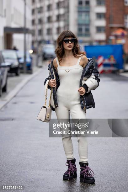 Lea Naumann wears full Louis Vuitton, creme white overall, down feather jacket, bag, laced snow boots, earrings & sunglasses on November 27, 2023 in...