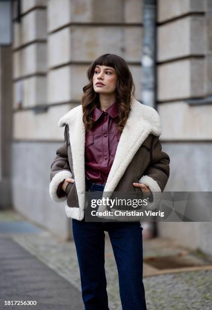 Lea Naumann wears Gant shearling jacket, burgundy button shirt, flared denim jeans, boots on November 27, 2023 in Berlin, Germany.