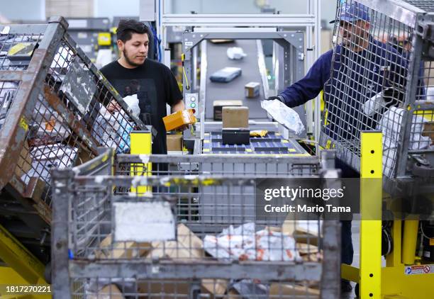 Postal Service employees Cesar Chavez and Gilbert Gonzalez place packages into a new package sorting machine, which can process up to 3,000 packages...