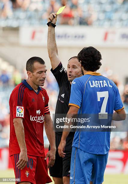 Referee Mateu Lahoz shows the yellow card to Patxi Punal of CA Osasuna after a fault to Getafe CF player Sergio Escudero in company of his teammate...