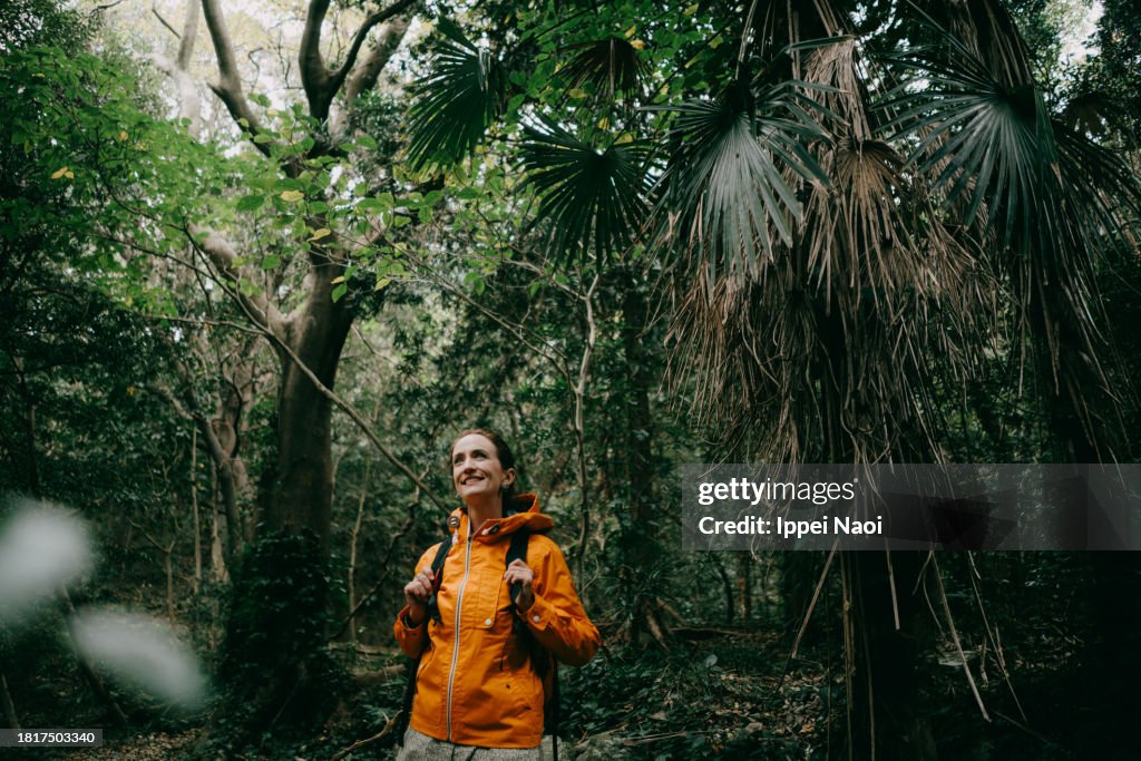 Woman in orange outdoor jacket, hiking in forest