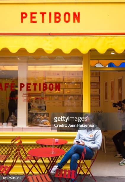 paris, france: man sits with phone outside petitbon cafe - window awnings bildbanksfoton och bilder