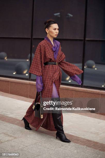 Guest wears purple tights, a brown long coat, and black long leather boots during the Tashkent Fashion Week 2023 on November 27, 2023 in Tashkent,...