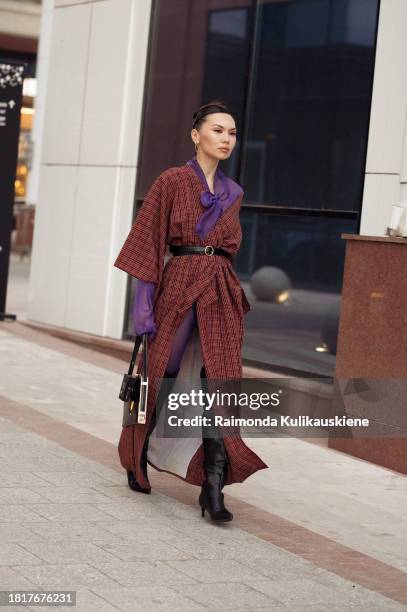 Guest wears purple tights, a brown long coat, and black long leather boots during the Tashkent Fashion Week 2023 on November 27, 2023 in Tashkent,...