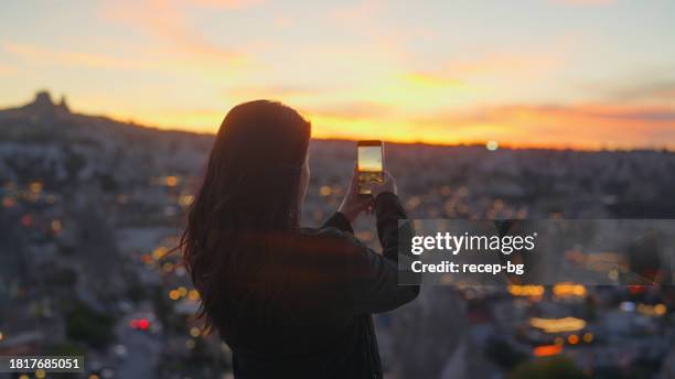 multiracial female tourist using her mobile smart phone to take photos of sunset from top of hill in cappadocia türkiye turkey - göreme national park stock pictures, royalty-free photos & images