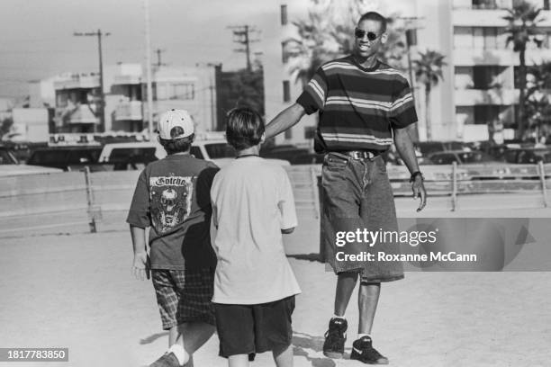 Reggie Miller of the Indiana Pacers wears a striped t-shirt, knee-length jeans, sunglasses and Nike shoes as he reaches out to shake the hand of a...