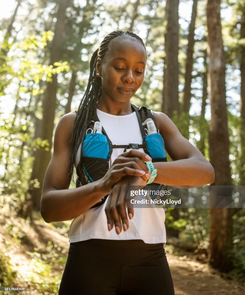 Mujer corredora comprobando los resultados en un reloj inteligente después de entrenar en el bosque