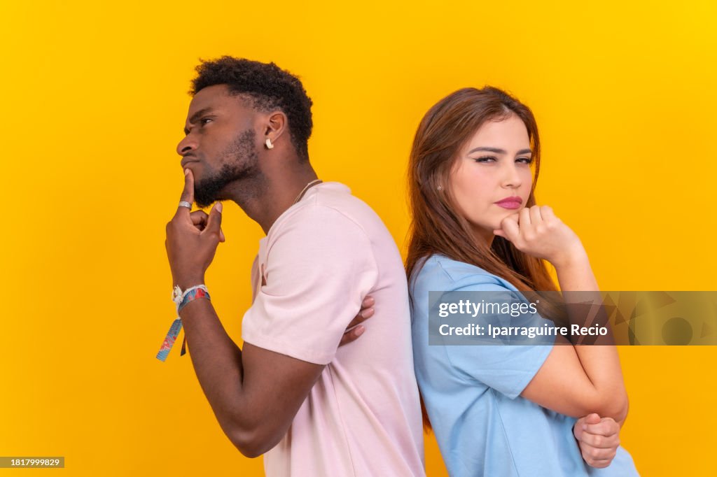 Two multi-ethnic young friends standing back-to-back hesitating