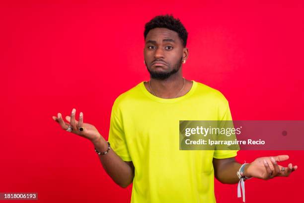 a young african man standing and shrugging - shrugging stock pictures, royalty-free photos & images