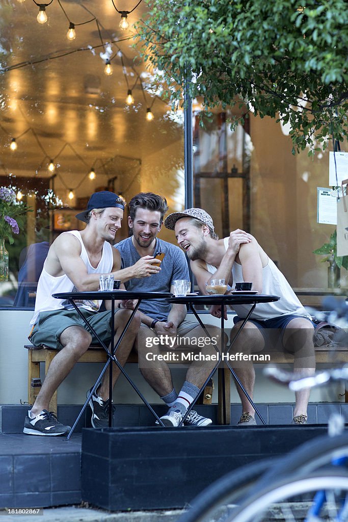 Three oyung men looking at phone outside cafe