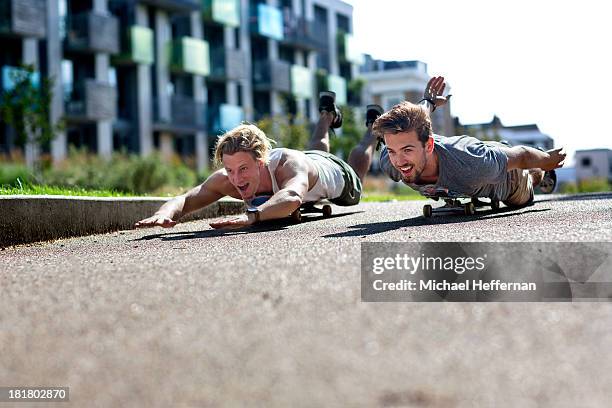 two young men lying on skate boards and racing - allongé sur le devant photos et images de collection