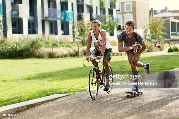 male cyclist and skateboarder in park - skateboard bike stock pictures, royalty-free photos & images