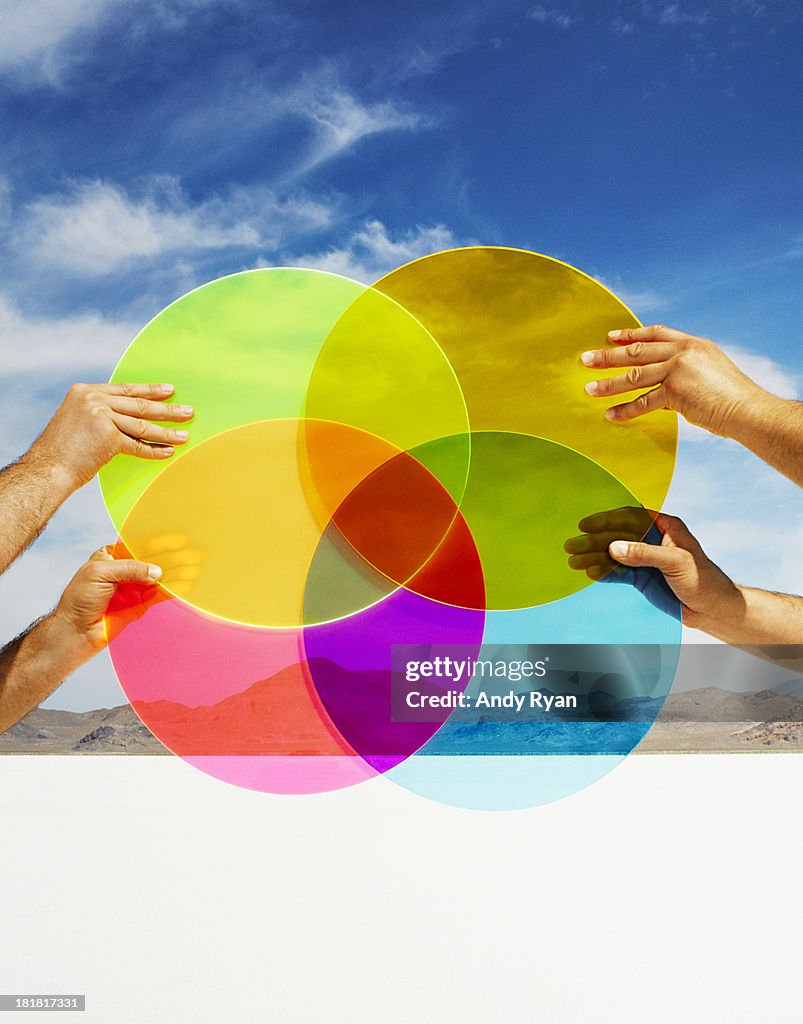 Hands holding multi-colored discs in landscape.