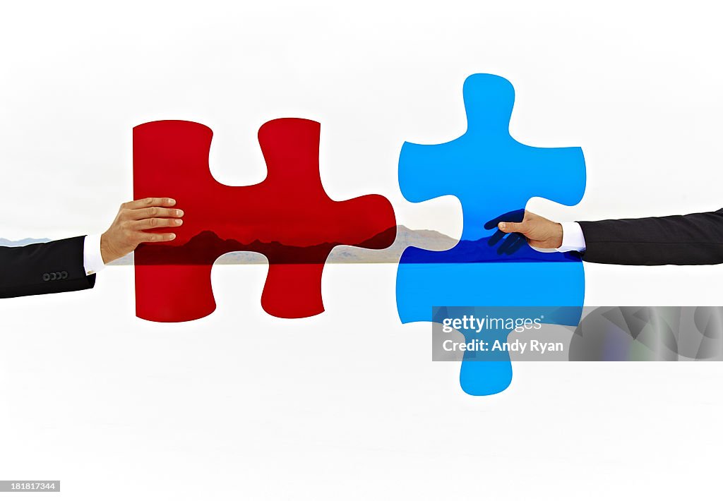 Two hands join colored puzzle pieces.