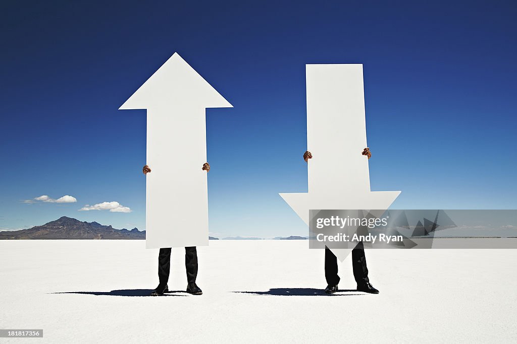 Two men holding giant arrows in desert.