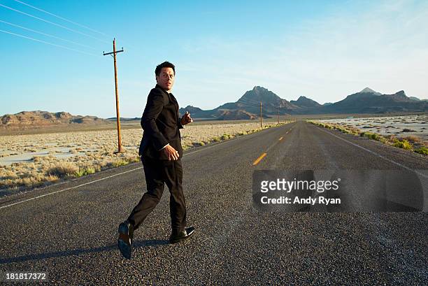 businessman running down desert road, looking back - fuggire foto e immagini stock