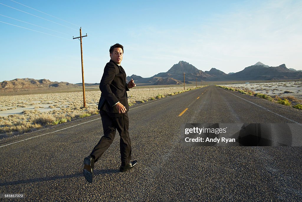 Businessman running down desert road, looking back