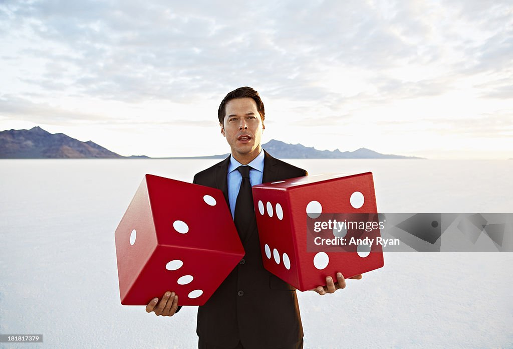 Businessman holding giant dice in desert.