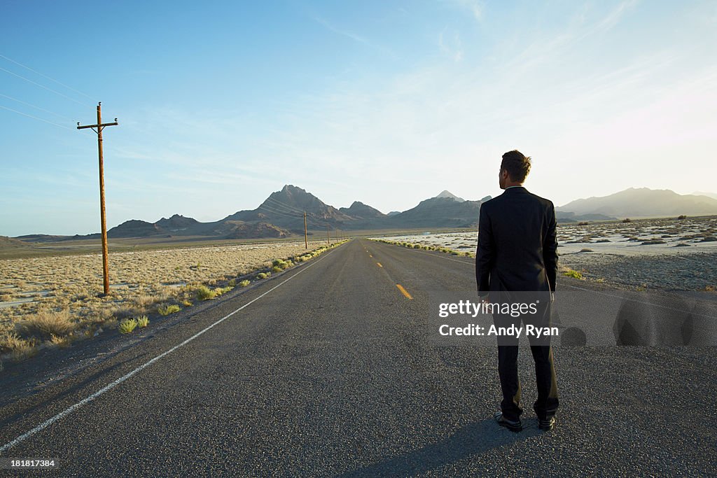 Businessman standing in desert road, looking ahead