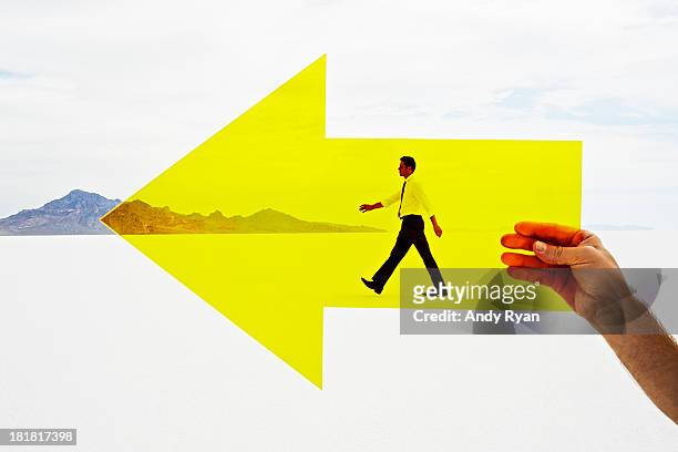 hand holding arrow with man walking in background. - direction concept stock pictures, royalty-free photos & images