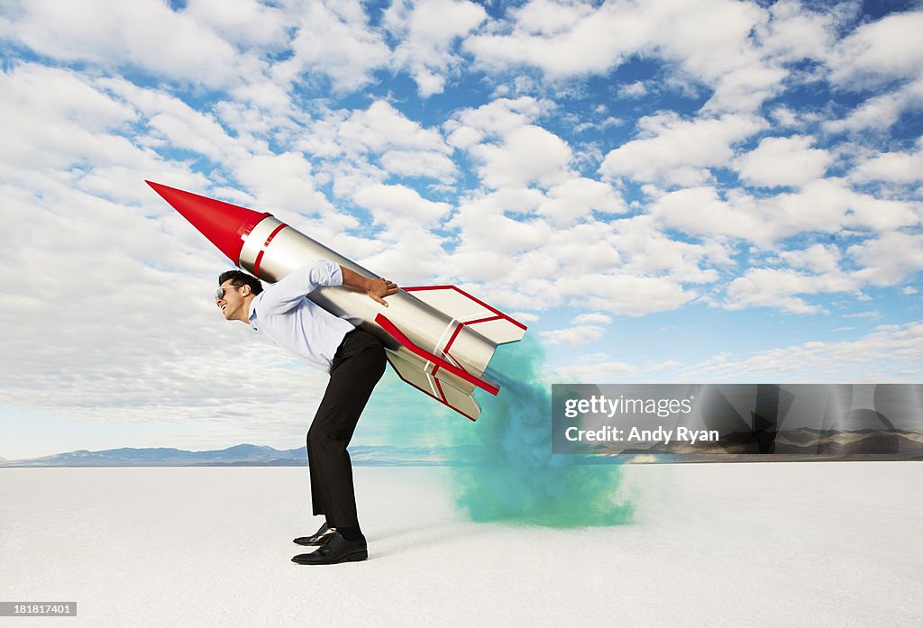 Man holding rocket on his back in desert.