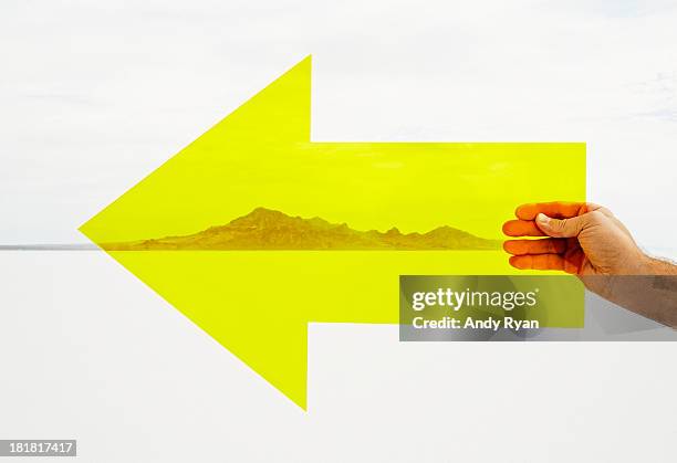 hand holding yellow arrow in desert. - clear direction stock pictures, royalty-free photos & images