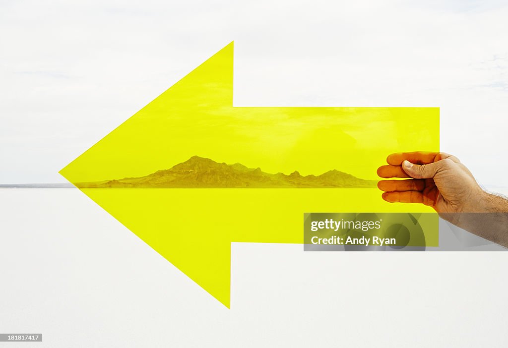 Hand holding yellow arrow in desert.